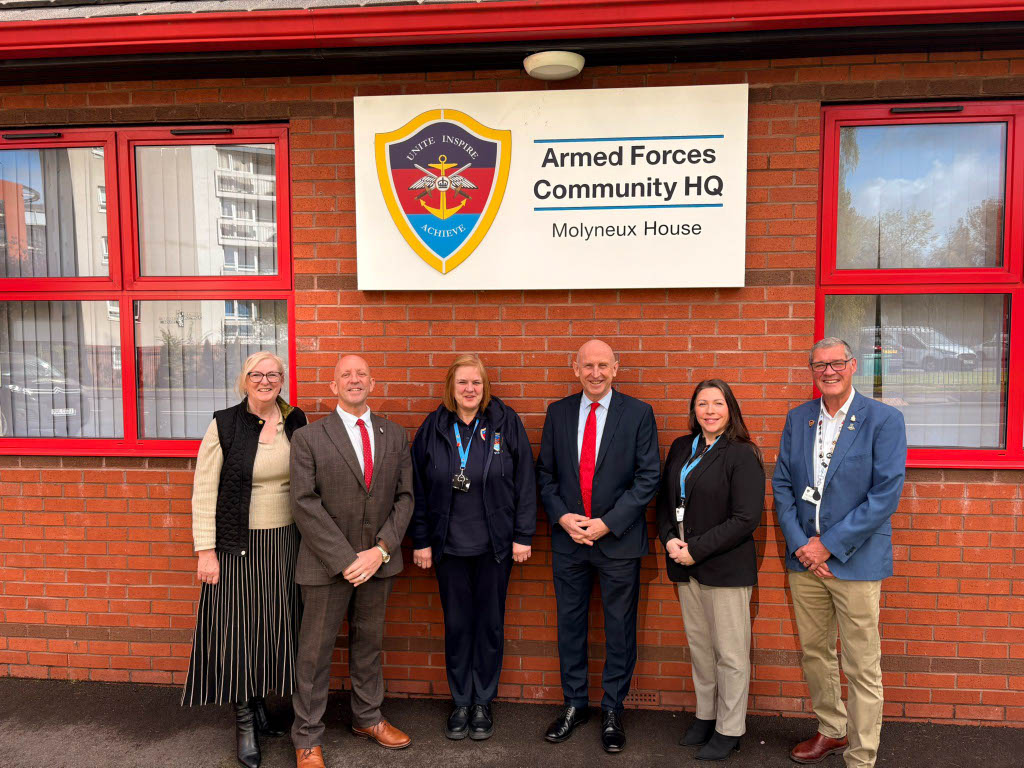 A group image of six individuals, standing in front of the Armed Forces Community HQ sign in wigan.